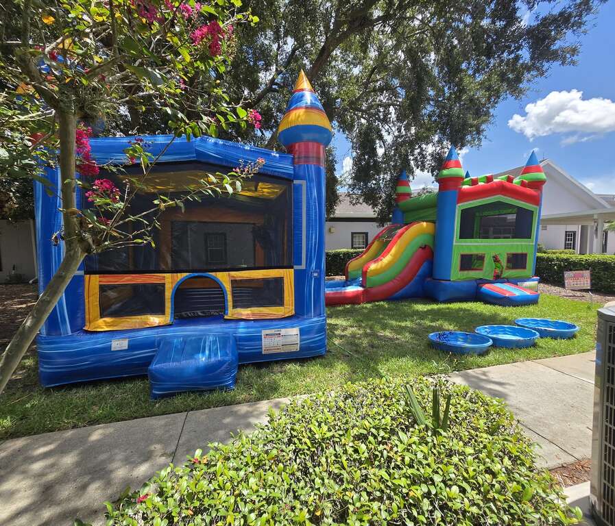 Blue castle bounce house and a castle combo with slide set up on grass beside a church in Saint Cloud, FL