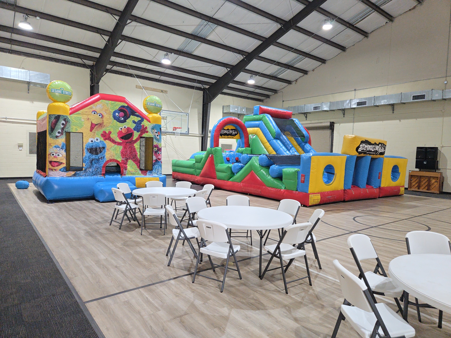 Obstacle course, bounce house and round-table seating set up inside a gym for an indoor event