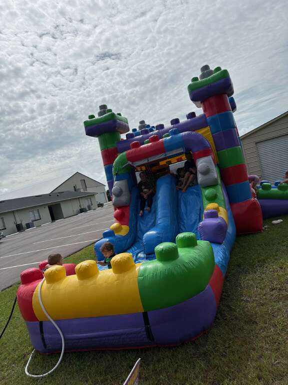 Mega Block Double Lane Combo with twin slides and a splash pool set up on the grass beside a church parking lot, with children playing on it