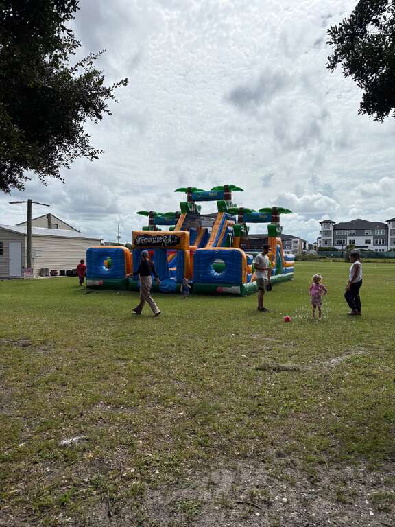 Adrenaline Rush 2 Obstacle Course with palm tree tops set up on an open grass field, with families walking toward it