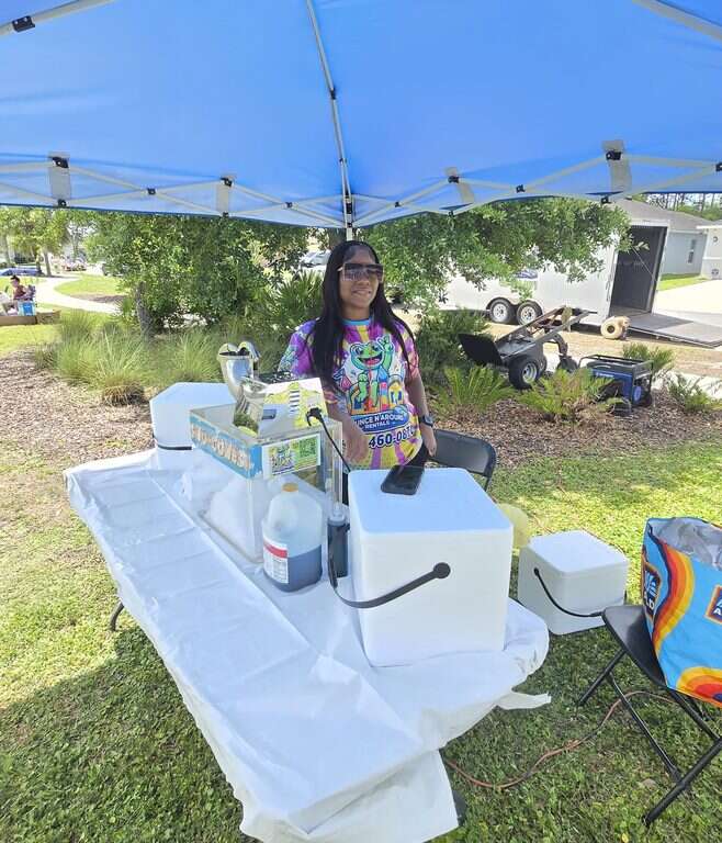 Bounce N Around Rentals staff member at the snow cone machine under a canopy at a Tivoli Reserve community event in Davenport, FL