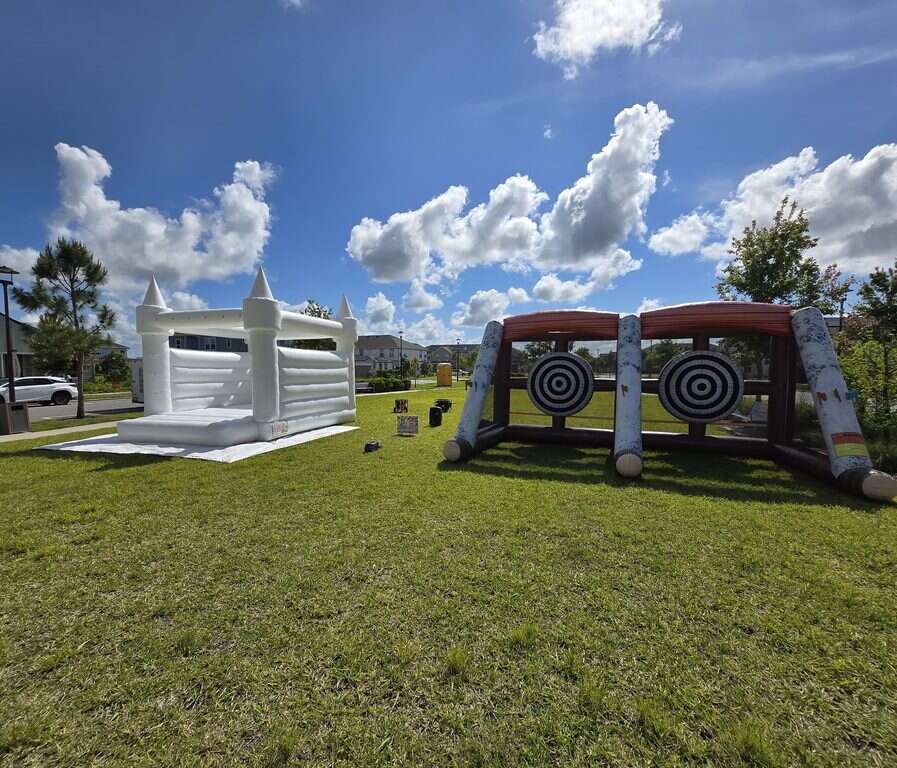 White bounce house and double axe throw game set up on the lawn at Pioneer Park for the Weslyn Park HOA community event in Saint Cloud, FL