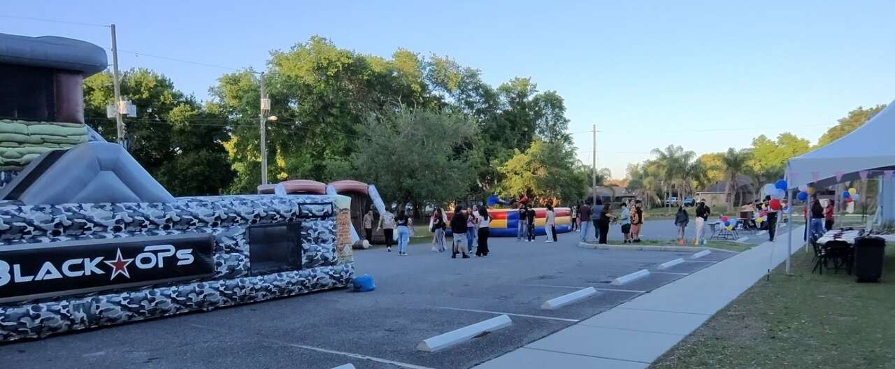 Black Ops Obstacle Course on a church parking lot in Saint Cloud, FL, with a Joust arena and a white high-peak tent behind it during an evening youth outreach