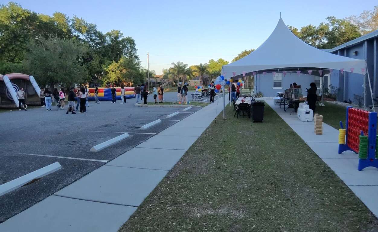 White high-peak tent with concessions, an axe throw game, a Joust arena and giant yard games set up at a church youth event in Saint Cloud, FL