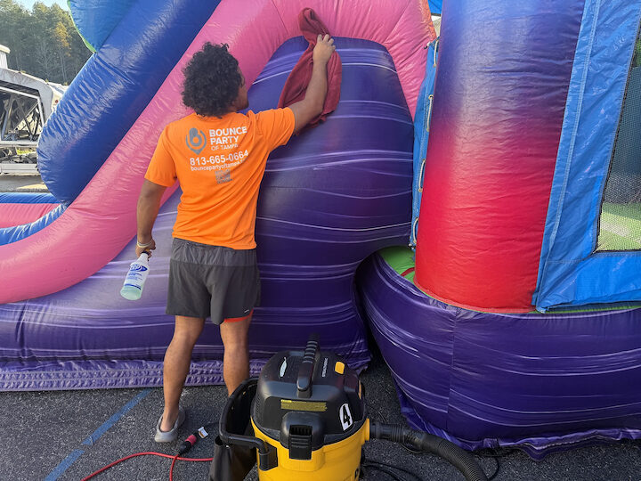A crew member wiping down an inflatable slide with sanitizer, a shop vacuum at his feet