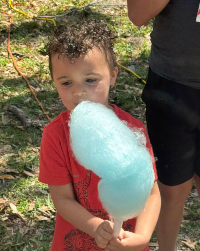 A little boy in a red T-shirt holding a big blue cotton candy at an outdoor party