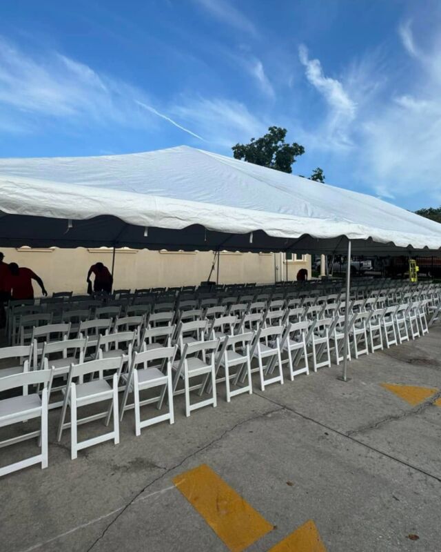 A frame tent shading rows of white folding chairs, set up for an outdoor event