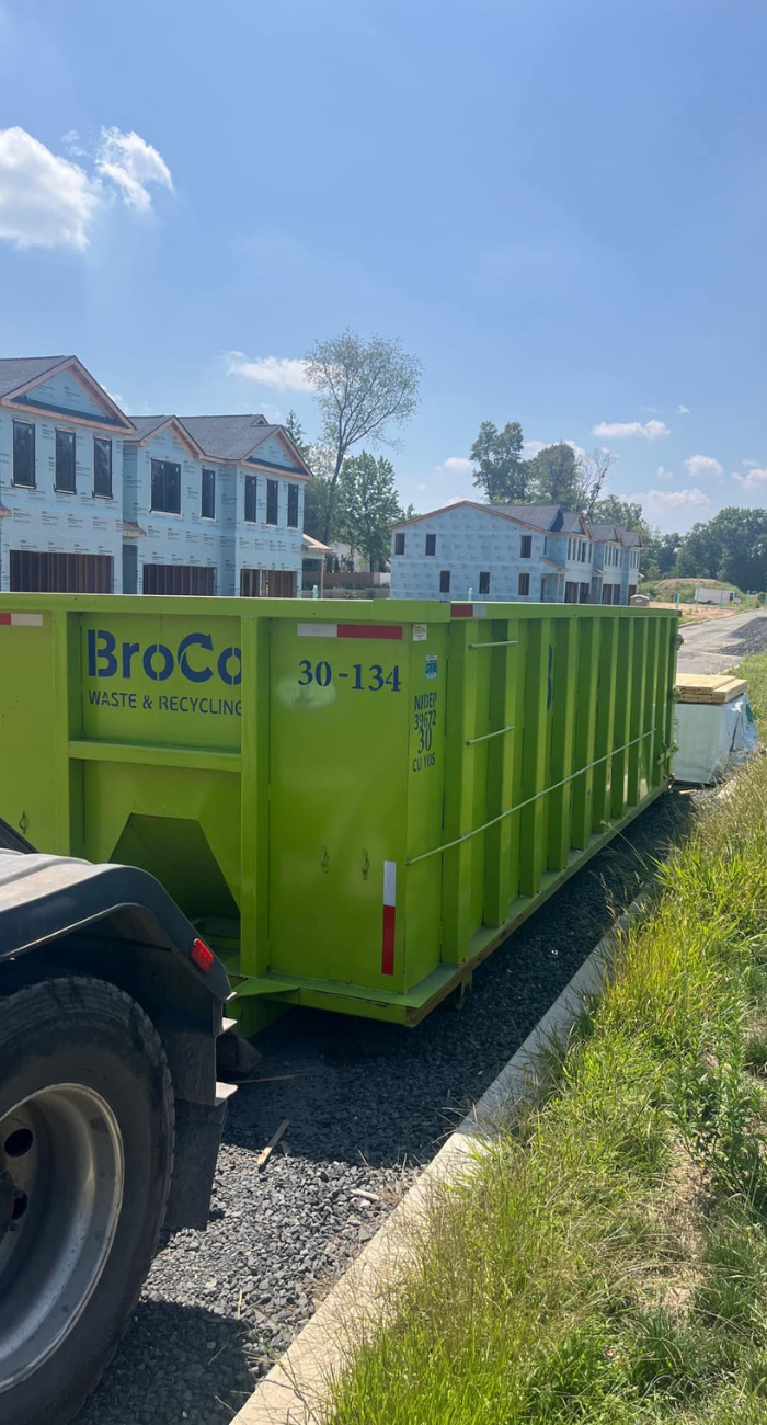 Bright green Broco Waste dumpster being delivered to a new construction site.
