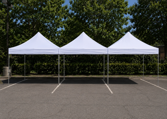 Three white high peak canopy tents set up side by side in a parking lot
