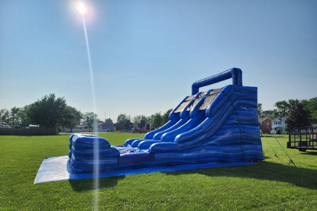 Large blue inflatable water slide set up beside building on grassy field area