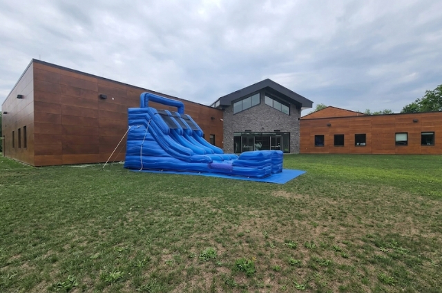 Large blue inflatable water slide set up beside building on grassy field area