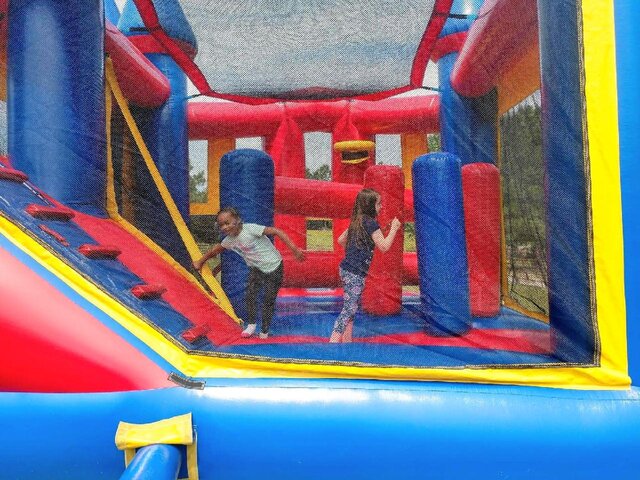 Two girls jump inside of a blue and red bounce house combo with slide and obstacles
