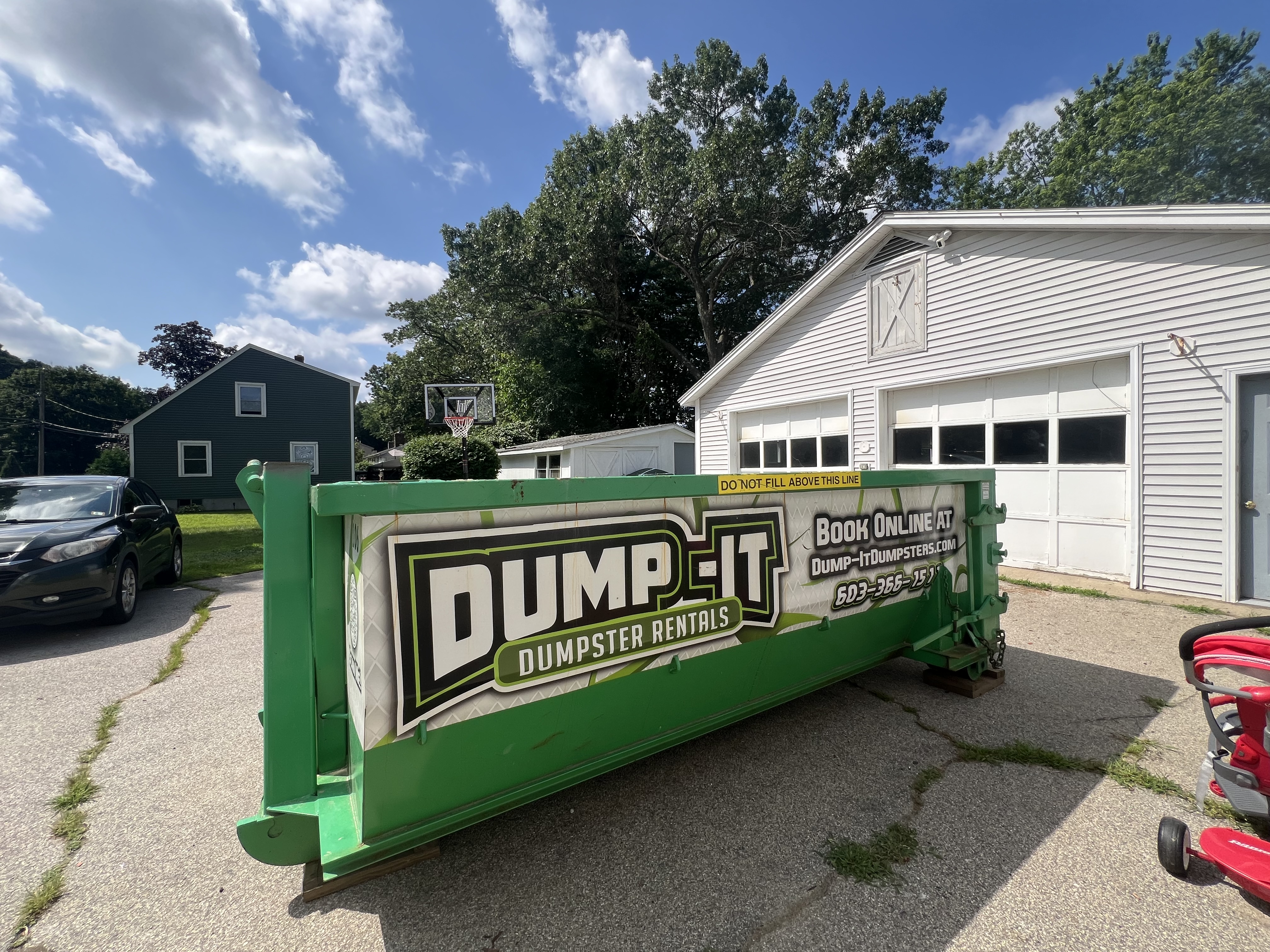 Dump-It Dumpster Rentals logo over a driveway dumpster at night.