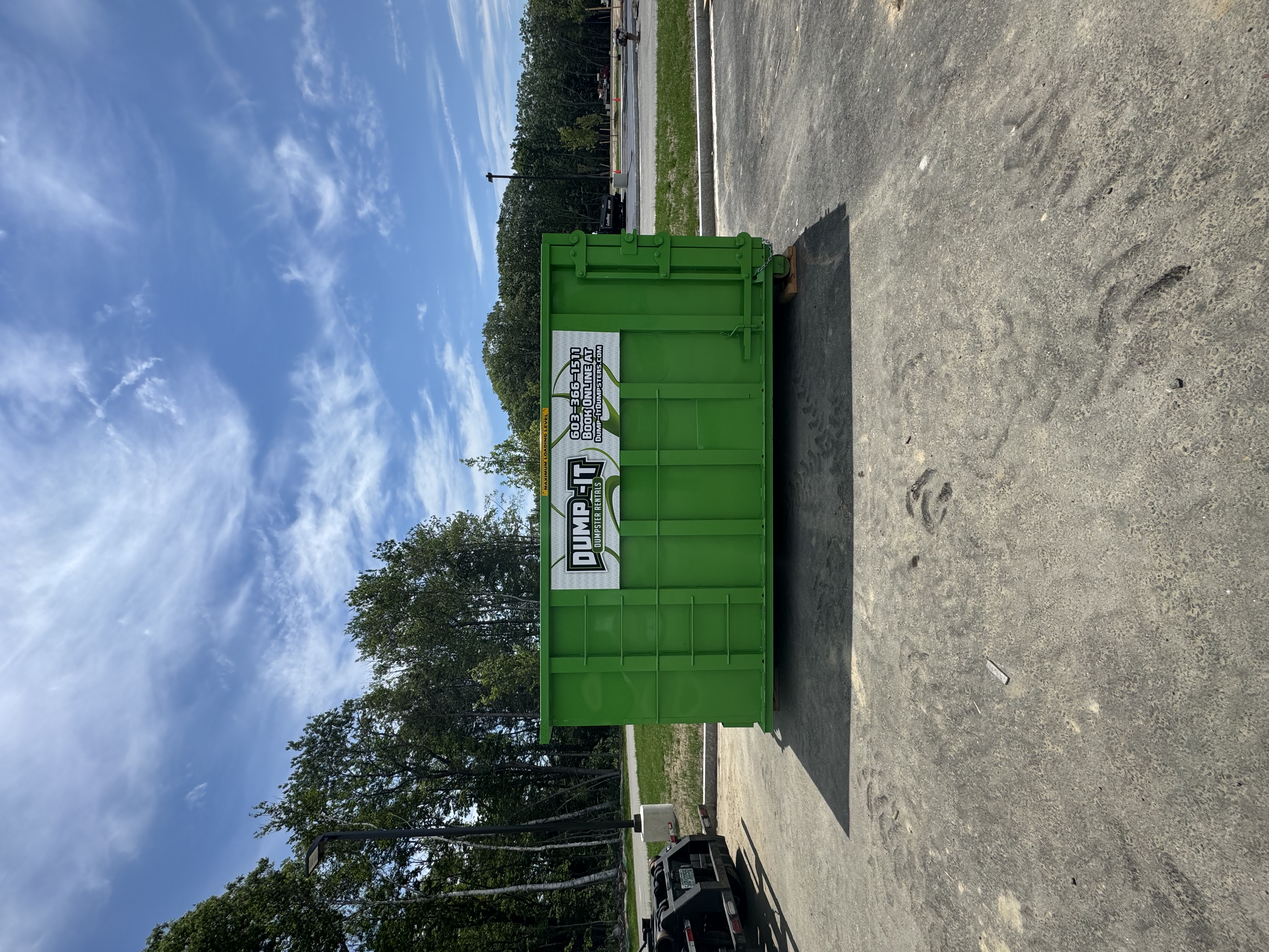 Dump-It Dumpster Rentals logo over a driveway dumpster at night.