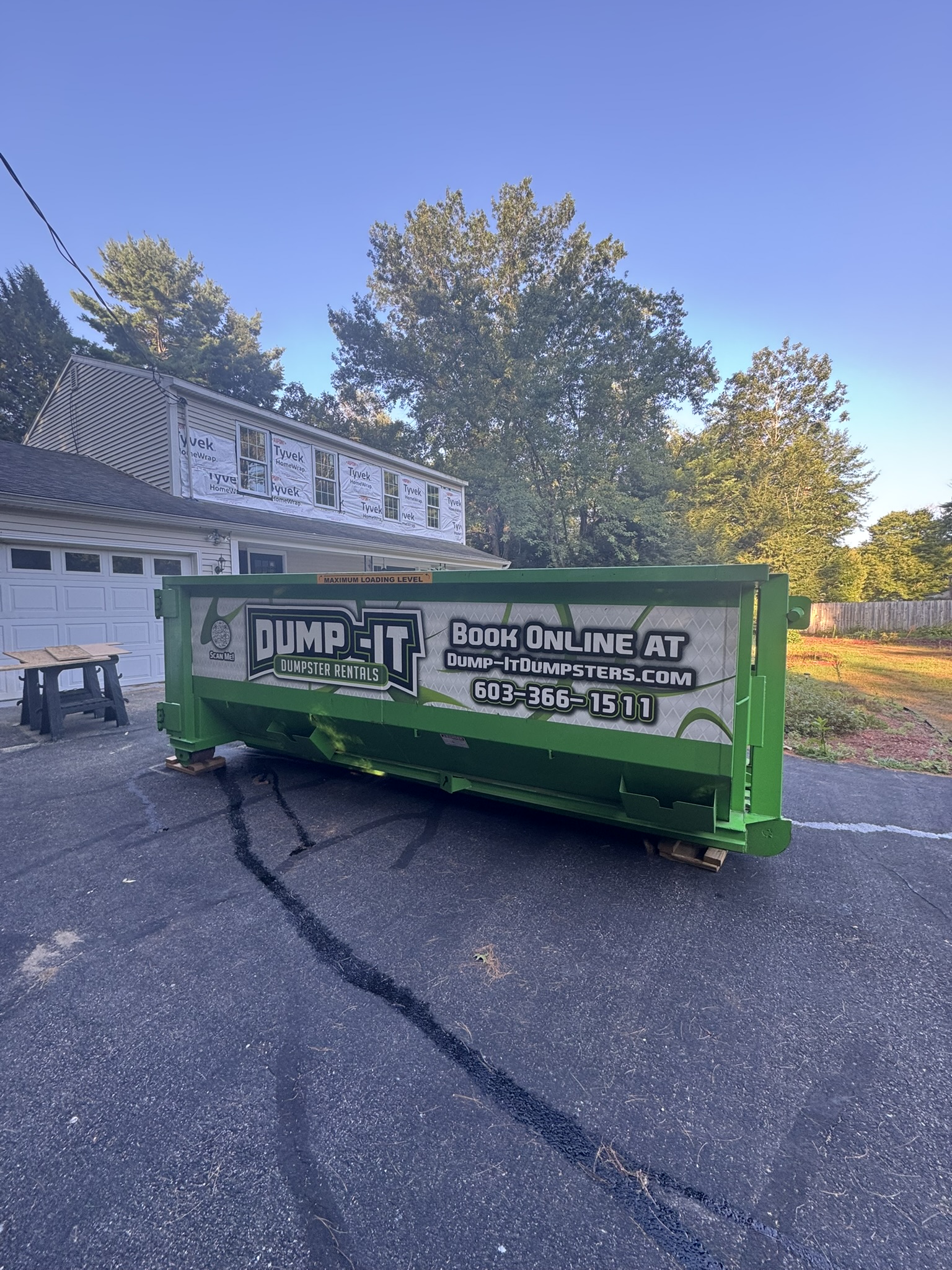 Dump-It Dumpster Rentals logo over a driveway dumpster at night.