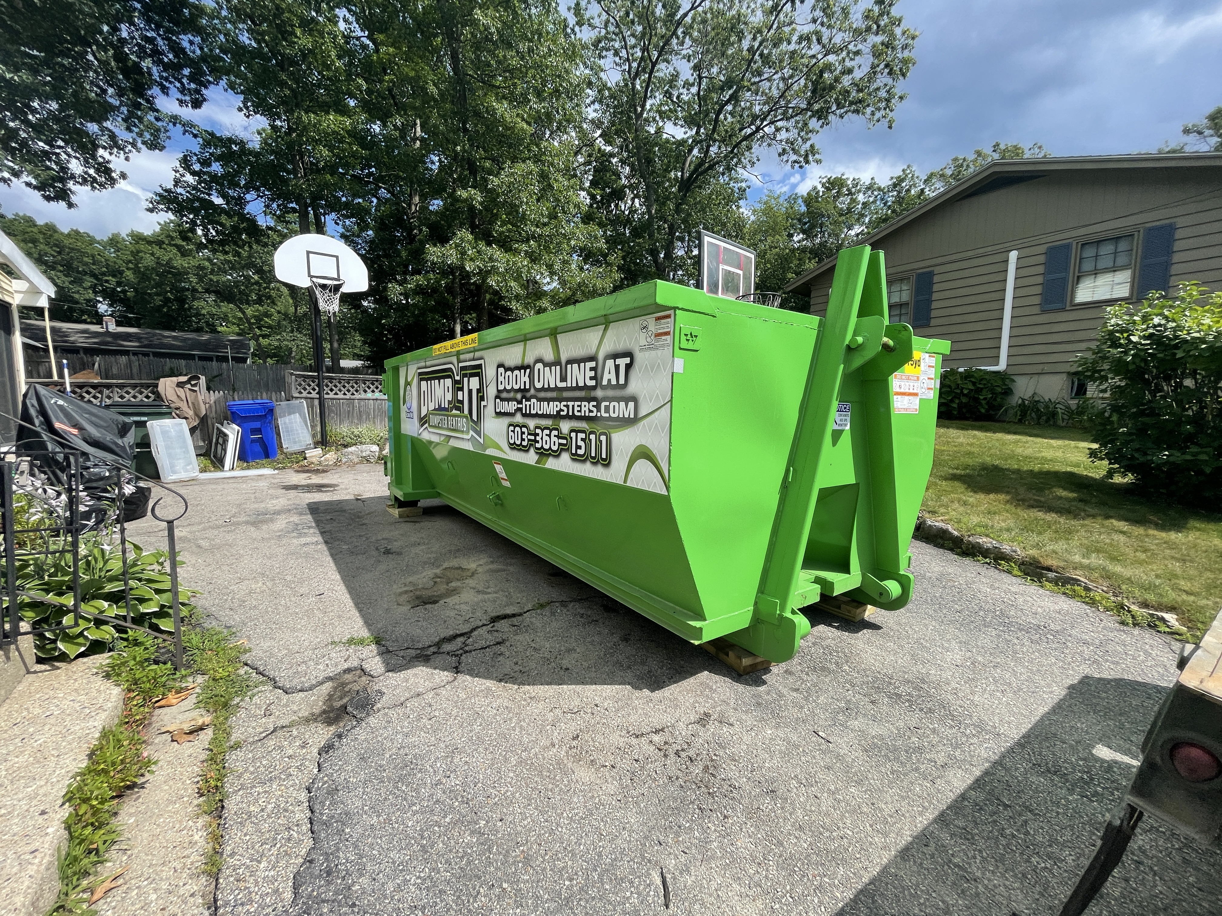 Dump-It Dumpster Rentals logo over a driveway dumpster at night.
