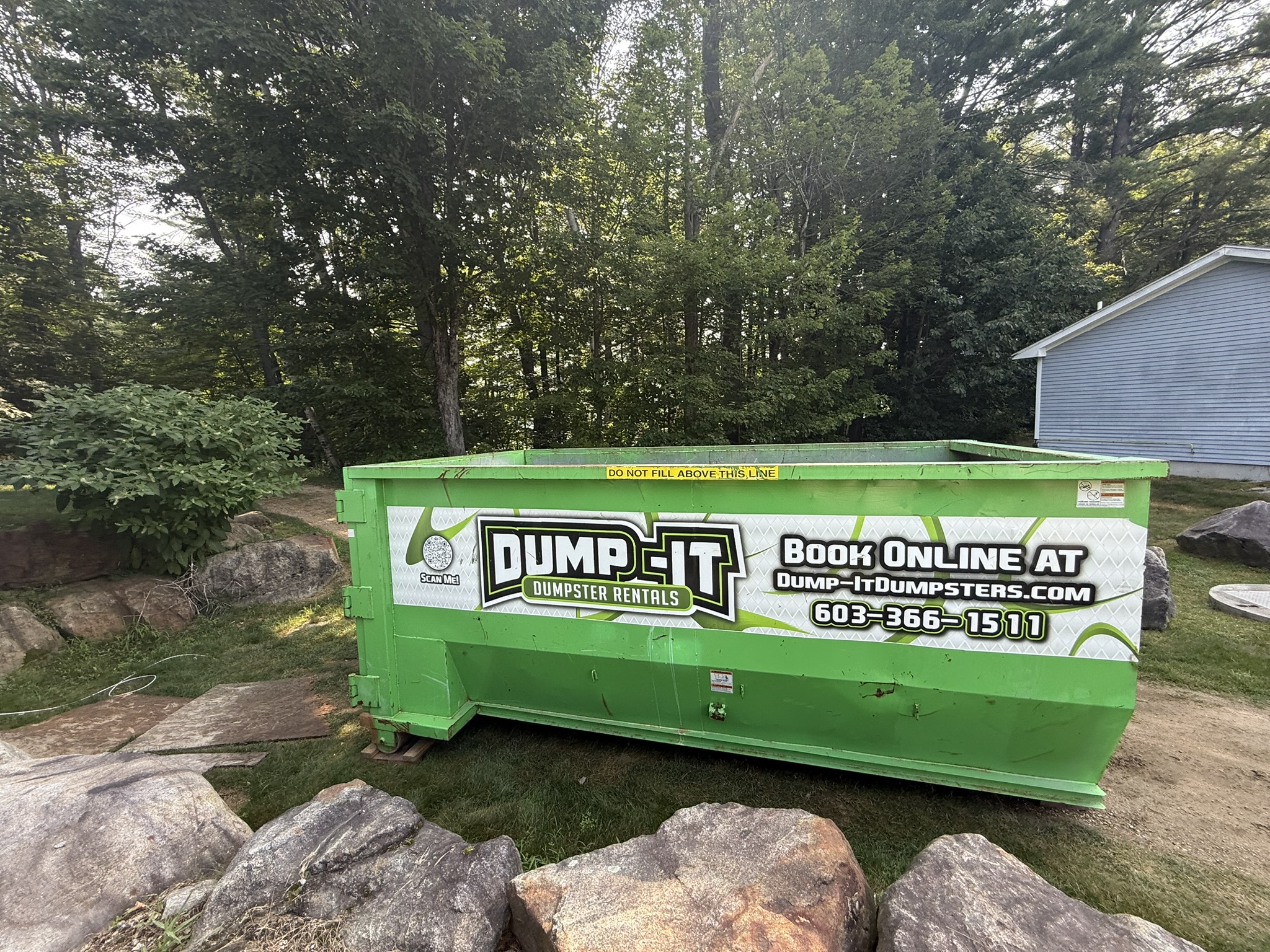 Dump-It Dumpster Rentals logo over a driveway dumpster at night.