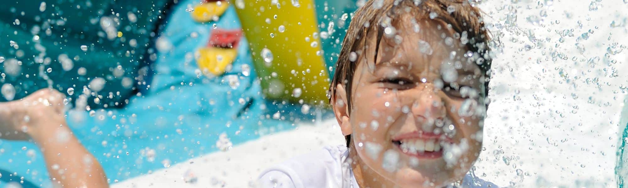 Smiling boy with water drops flying around him at an inflatable water slide party