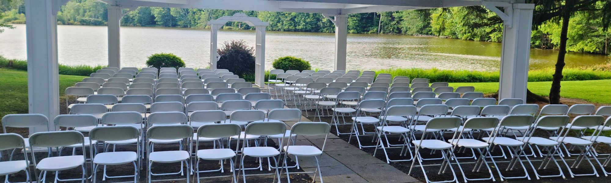 Rows of white folding chairs set up for an outdoor ceremony beside a lake