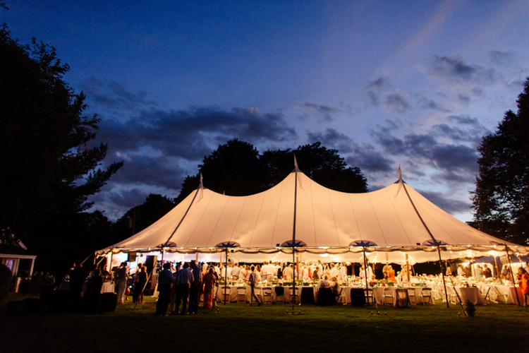 group of people gathered under a tent at sunset, having fun and enjoying themselves