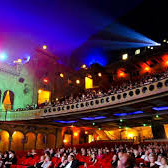 Theatres | Audience watching a play as colored lights shine from the tech booth
