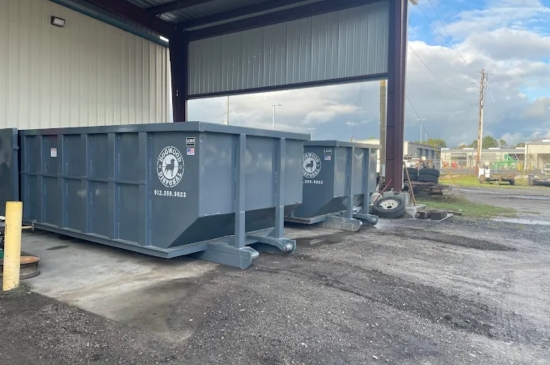Dogwood Disposal gray roll-off dumpsters parked under an open metal canopy beside a warehouse