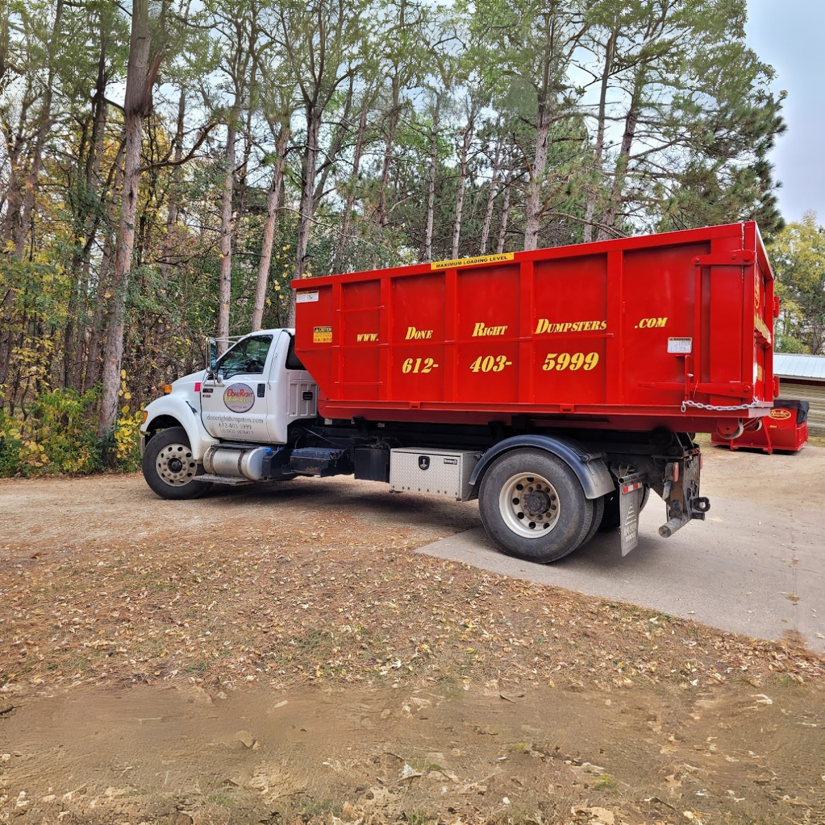 White and red roll-off truck from Done Right Dumpsters in a wooded area. White and red roll-off truck from Done Right Dumpsters in a wooded area.