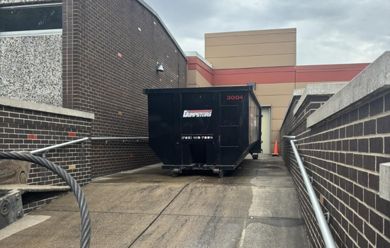 Large black dumpster positioned beside a brick commercial building Large black dumpster positioned beside a brick commercial building