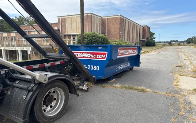 Roll-off dumpster being unloaded from a truck in a parking lot with Dumpster Pro NC