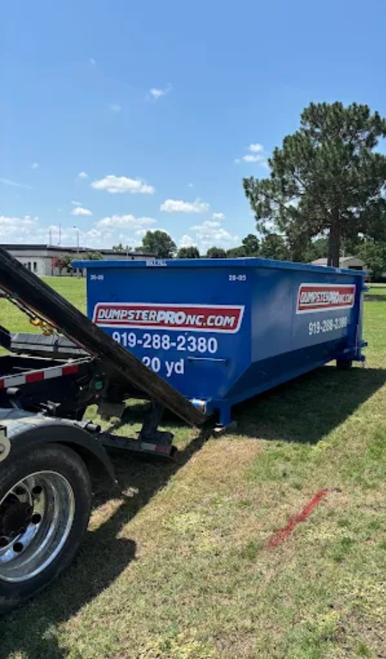 Blue 20-yard roll-off dumpster being delivered on a grassy lot by Dumpster Pro NC