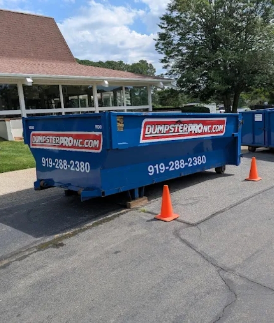 Blue roll-off dumpsters placed on a paved street with safety cones by Dumpster Pro NC