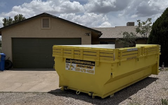 Yellow roll-off dumpster placed in a driveway for home cleanouts with Dutton Dumpsters