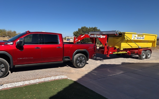 Red truck hauling a heavy-duty roll-off dumpster for construction waste by Dutton Dumpsters