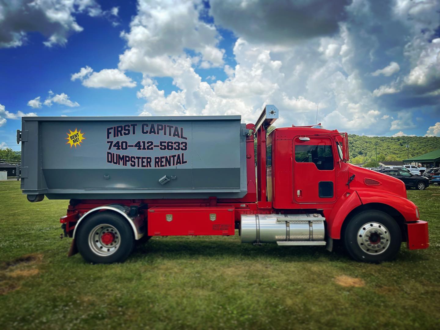 Red roll-off truck with First Capital Dumpster Rental container parked on grass Red roll-off truck with First Capital Dumpster Rental container parked on grass