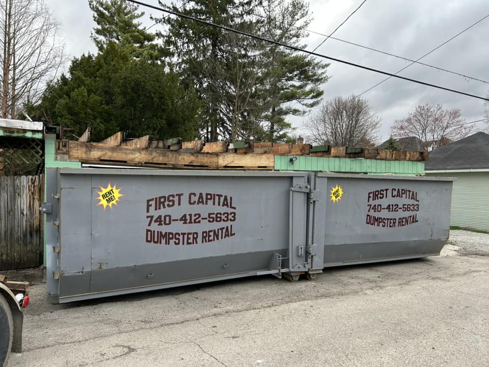 Gray dumpster from First Capital Dumpster Rental filled with construction debris at a job site. Gray dumpster from First Capital Dumpster Rental filled with construction debris at a job site.