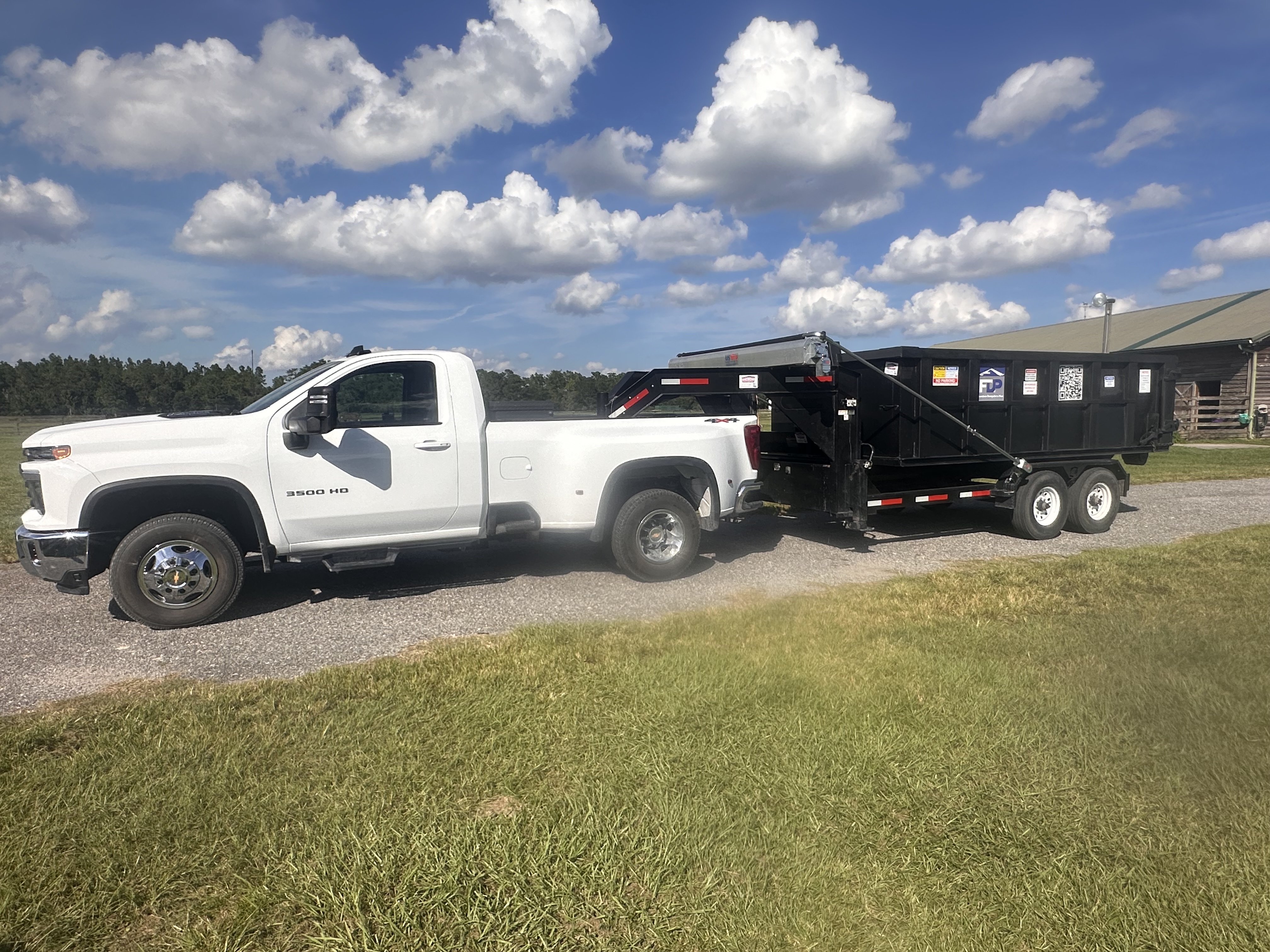 Freedom Dumpsters Plus black dumpster trailer hitched to white truck Freedom Dumpsters Plus black dumpster trailer hitched to white truck