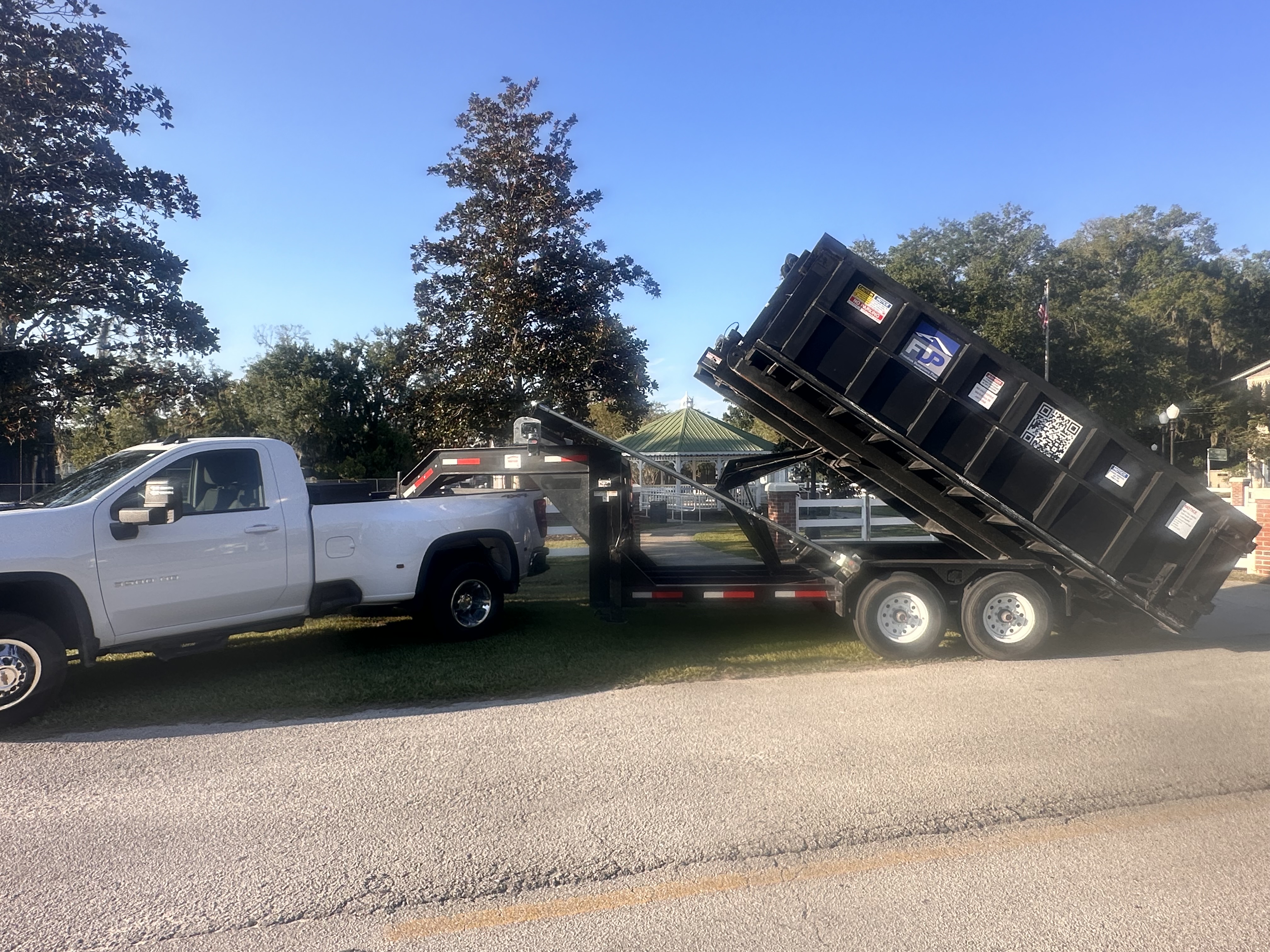 Freedom Dumpsters Plus trailer unloading black dumpster from white pickup truck. Freedom Dumpsters Plus trailer unloading black dumpster from white pickup truck.