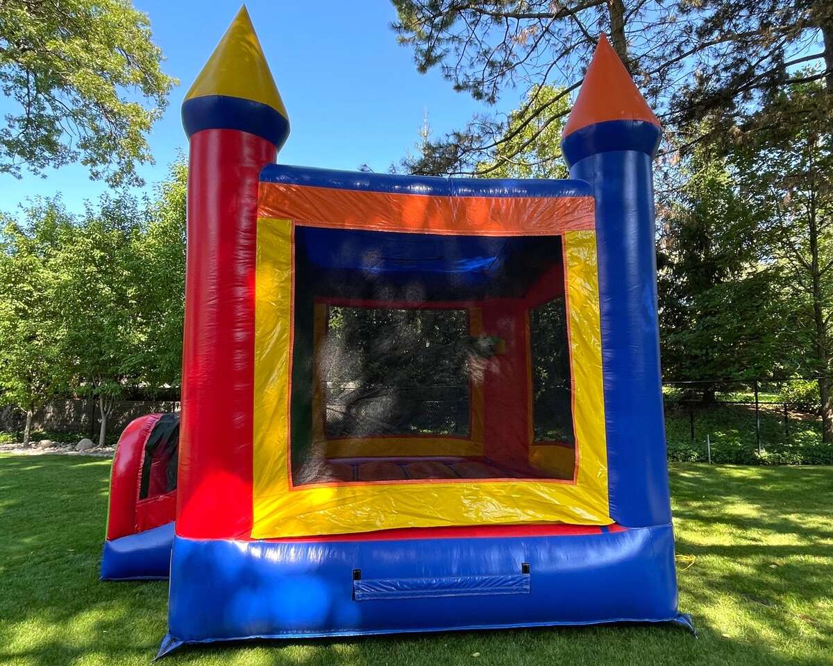 A colorful inflatable bounce house stands on a lush, sunlit lawn. Its vibrant red, blue, yellow, and orange panels evoke a fun, playful atmosphere.