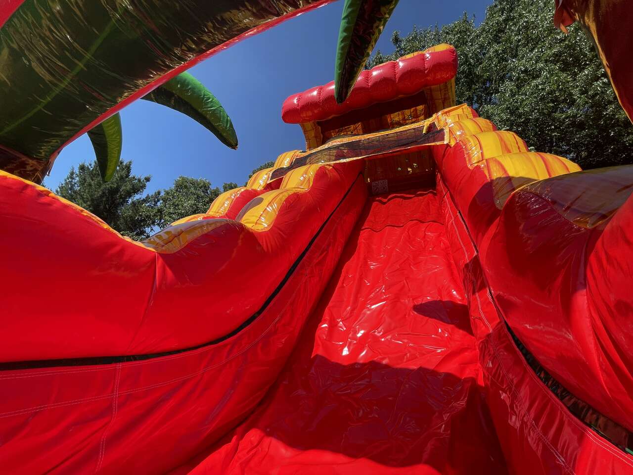 Close-up view of a bright red and yellow inflatable slide at an outdoor party or carnival attraction under a clear blue sky.