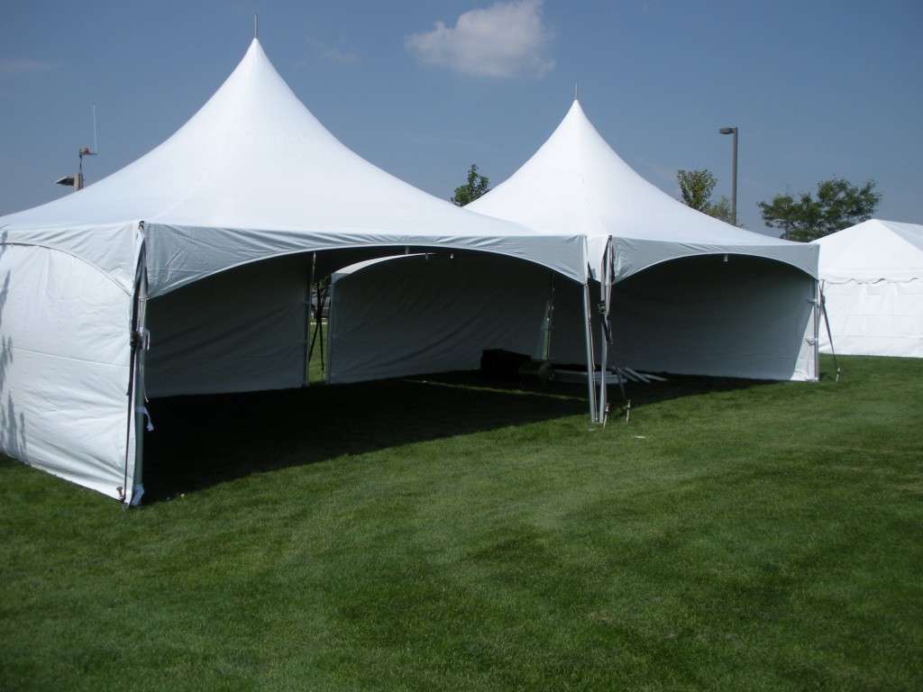 White high-peak event tents set up on a green grass field under a blue sky, featuring open sidewalls and spacious covered areas for outdoor weddings, corporate events, festivals, parties, and temporary event shelters. Large commercial canopy tents with elegant pointed tops arranged side by side in a sunny park setting.