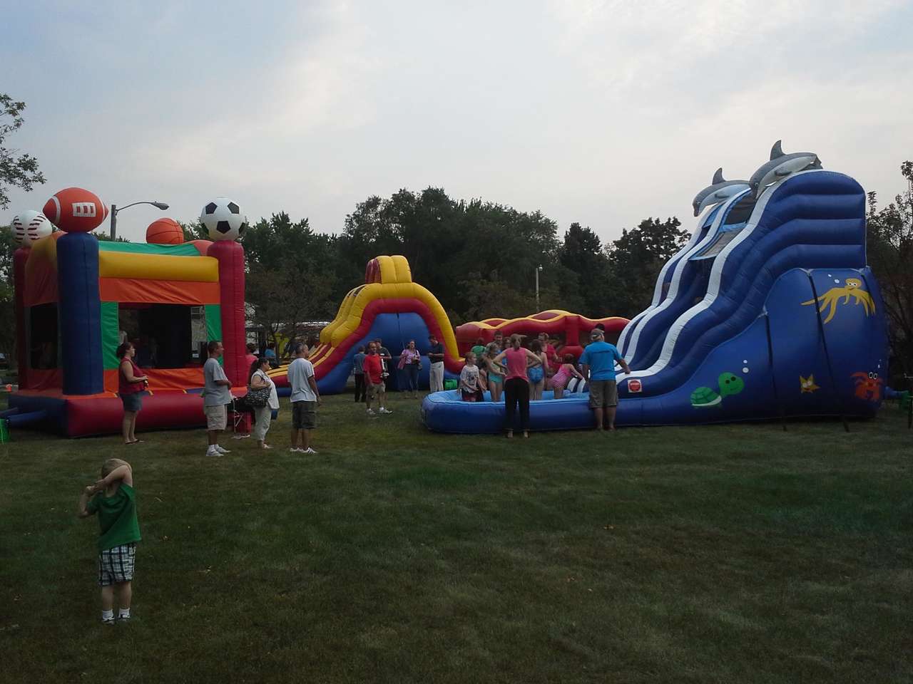 Outdoor inflatable playground with bounce houses, giant slides, and families enjoying a children’s party on a grassy field.