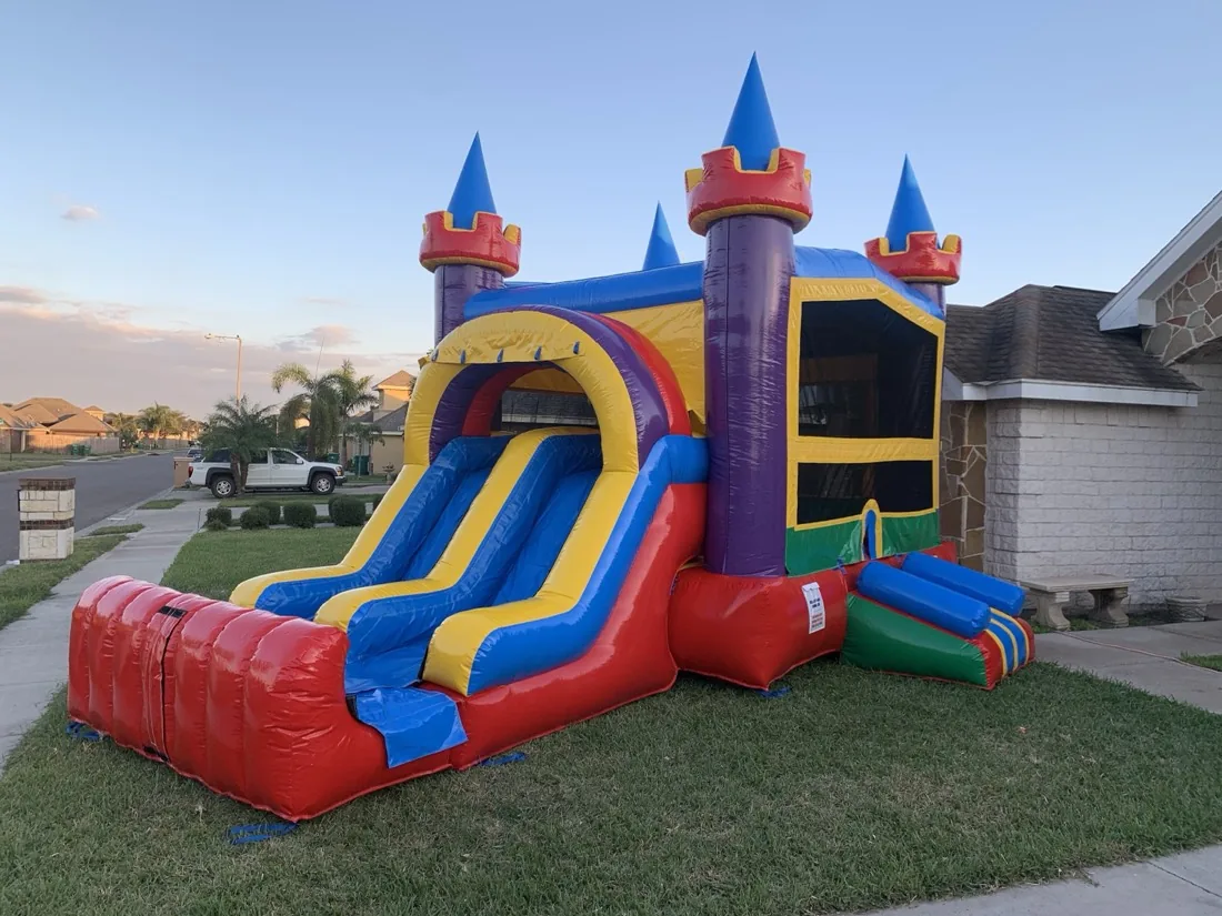 Red, yellow and blue castle bounce house with a double slide set up in a backyard