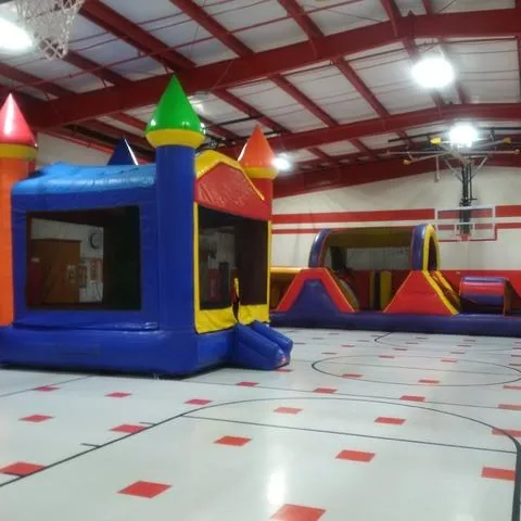 Castle bounce house and inflatable obstacle course set up inside a school gym