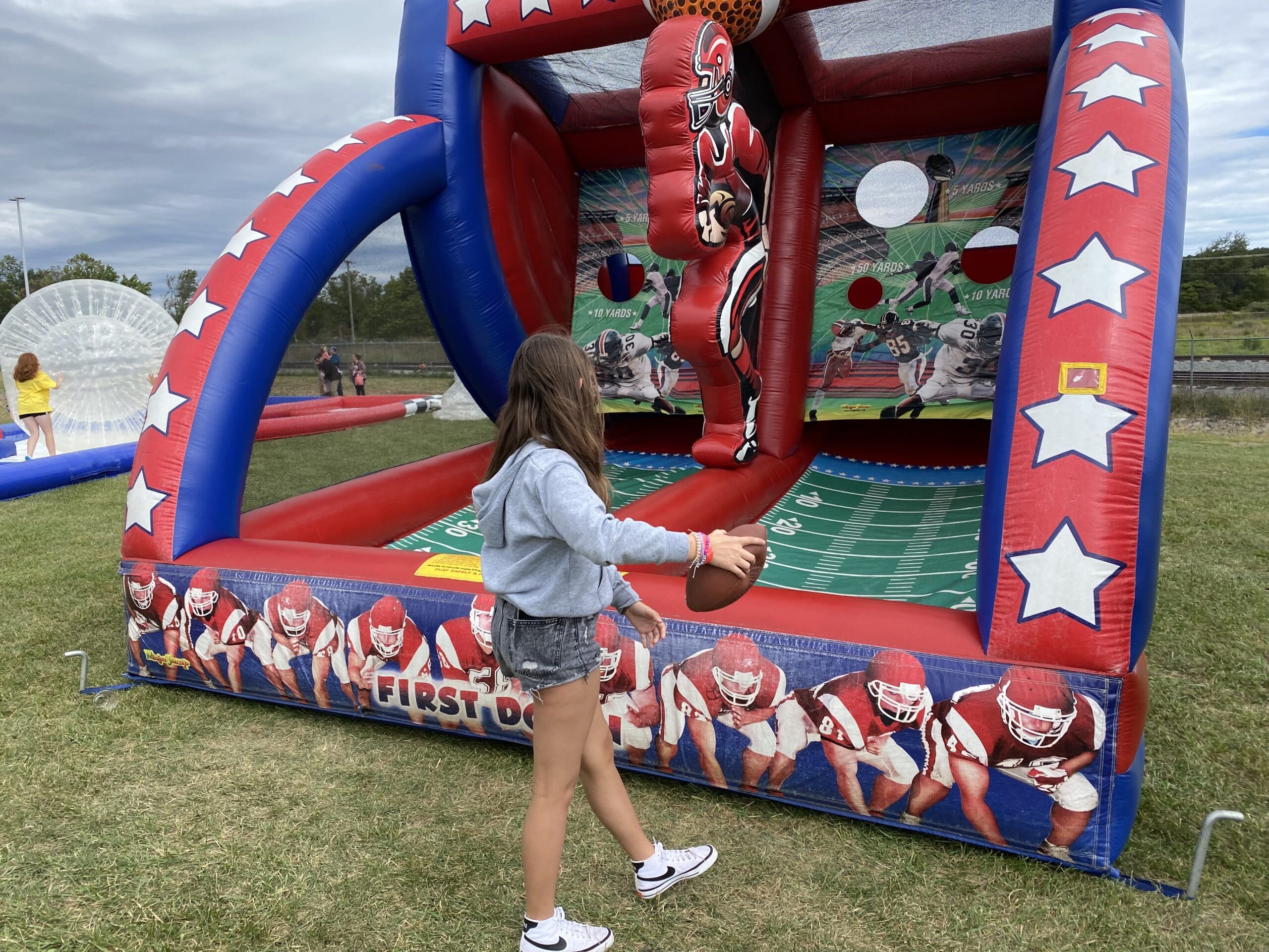 Girl preparing to throw a ball in a football inflatable game with vivid colors.