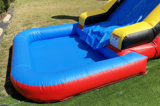 Close-up of an inflatable slide's blue and red landing pad on green turf, designed for safe, fun play.