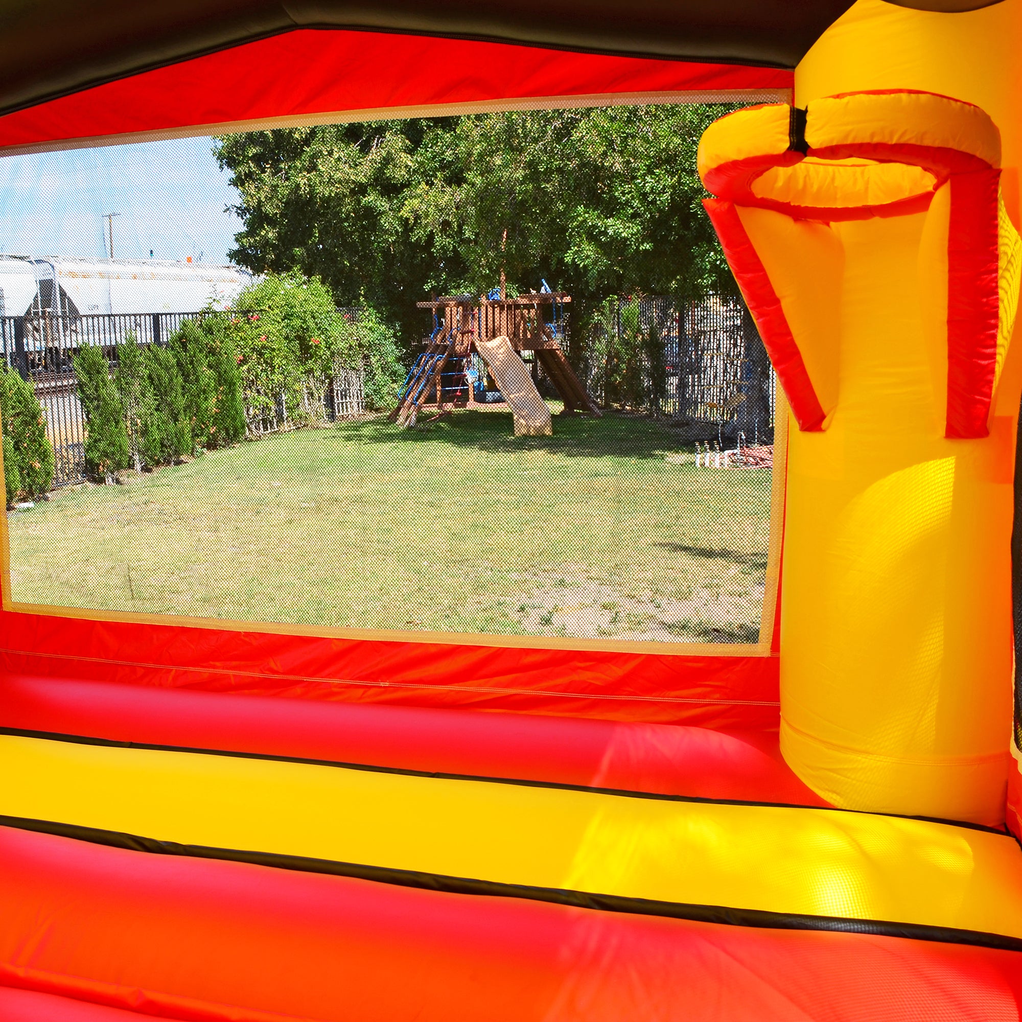 View through a bounce house window of a backyard playground and greenery.