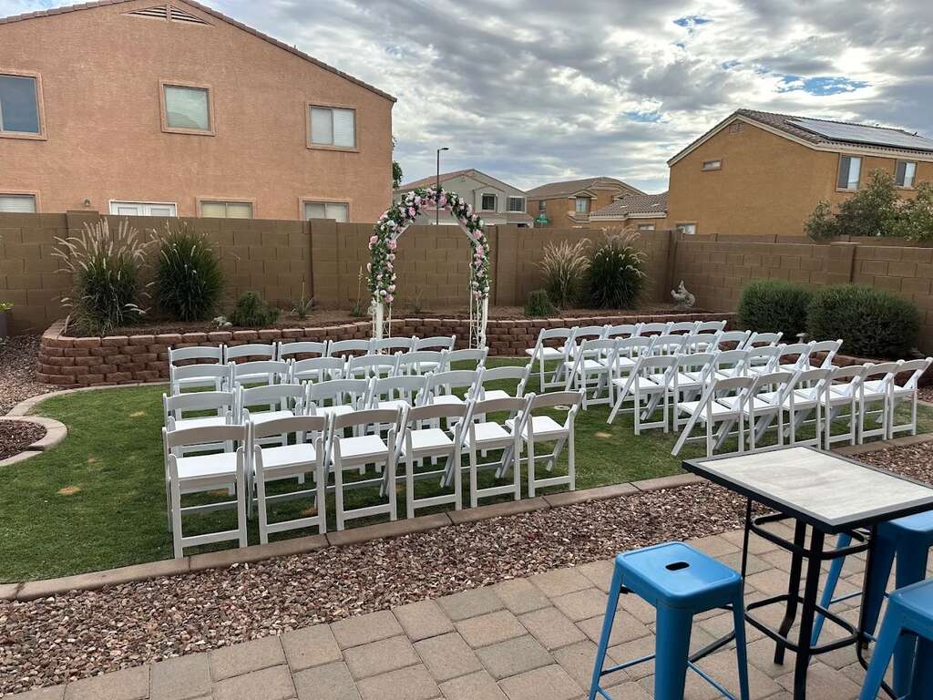 Complete backyard wedding party rental setup with white resin chairs floral ceremony arch and professional seating layout in Goodyear Arizona