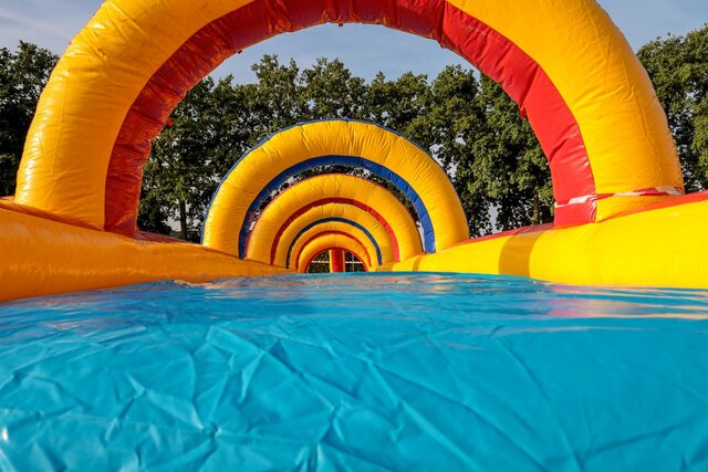 Low-angle view of a colorful inflatable bouncy castle with blue, red, and orange towers against a bright blue sky.