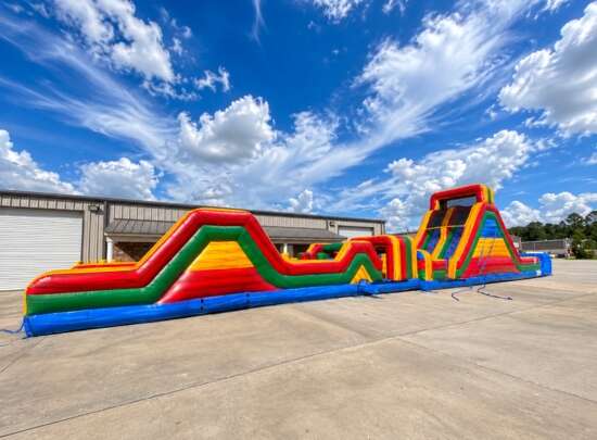 Colorful inflatable obstacle course with climbing walls and slides set up outdoors under a bright blue sky.