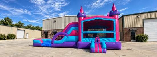 Pink and blue castle-themed combo bounce house with an attached slide and jumping area.
